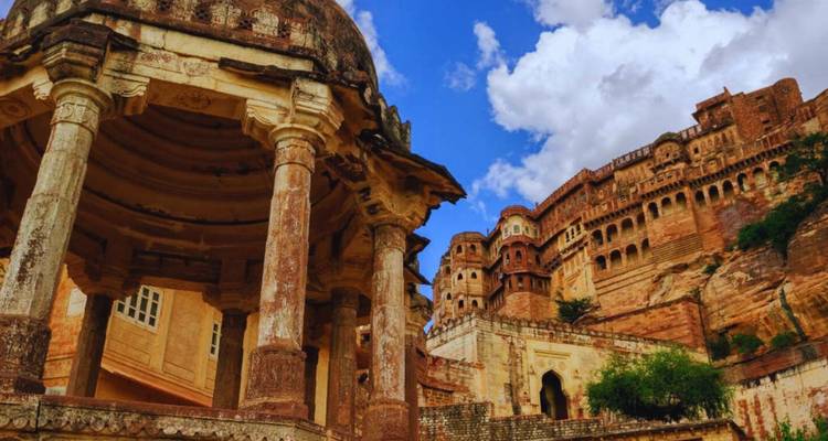 Verweerde zandstenen paviljoen en torenhoge vestingwerken van Mehrangarh Fort tegen een heldere hemel.