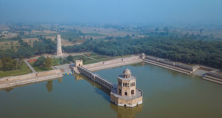 Vista aérea del pabellón Hiran Minar y el estanque de agua circundante en medio del campo brumoso.