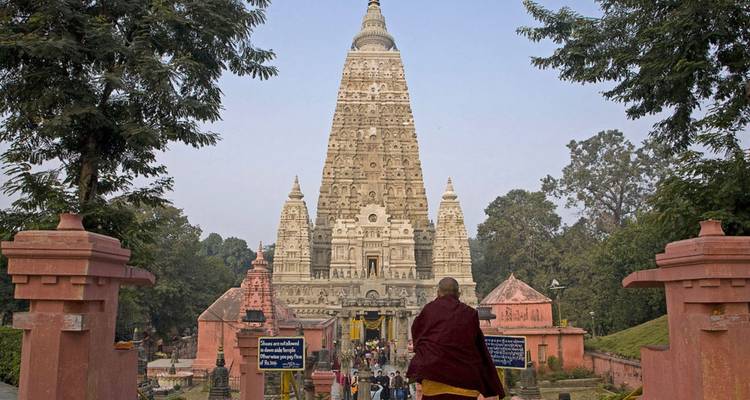 Los peregrinos se acercan al imponente Templo Mahabodhi en Bodhgaya enmarcado por árboles frondosos.