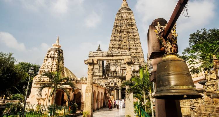 Vista lateral del complejo del Templo Mahabodhi con campana y pilares de piedra bajo un cielo brillante.