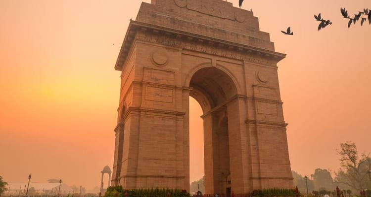 Puerta de la India silueteada en un cielo anaranjado y brumoso del amanecer con pájaros volando por encima.