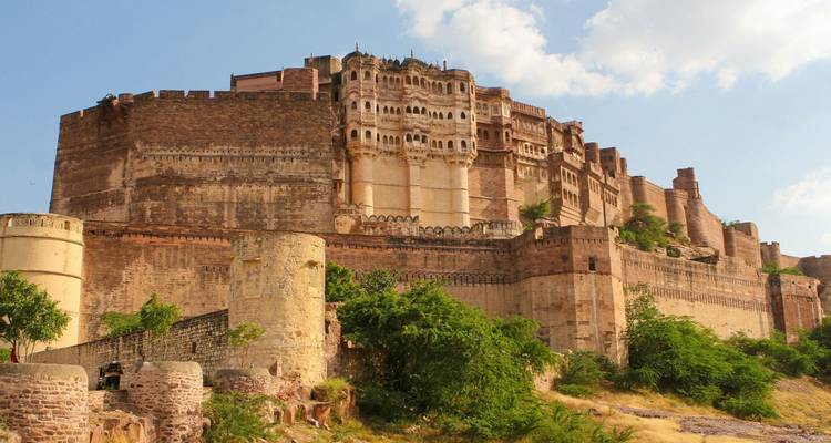 Des murs imposants et des créneaux du fort de Mehrangarh dominent une colline rocheuse sous un ciel bleu.
