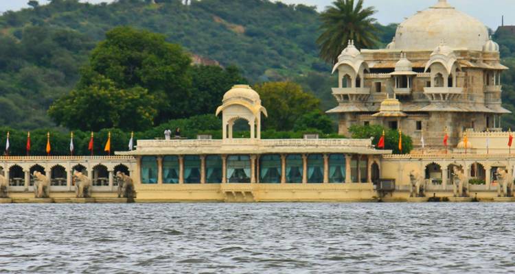 Pavillon colonial au bord du lac et bâtiments du palais vus à travers l'eau ondulante avec un arrière-plan de colline verte.