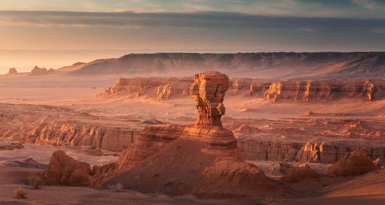 Pilier rocheux emblématique des falaises flamboyantes s'élevant au-dessus d'une vaste plaine aride à la lumière de l'aube.