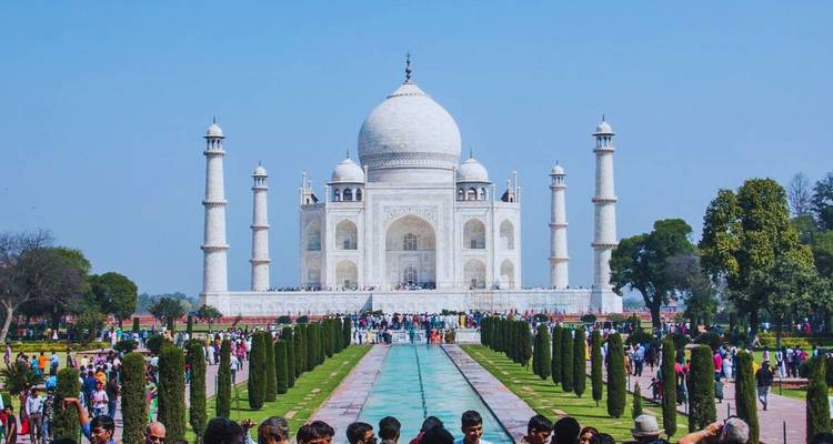 Menigten staan langs het lange waterkanaal dat leidt naar de glanzend witte Taj Mahal onder een heldere blauwe hemel.