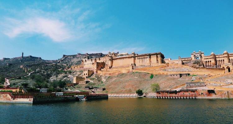 Uitgestrekt uitzicht op het amberkleurige Amer Fort dat zich uitstrekt over een ruige heuvelflank boven een gracht.