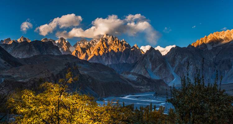 La lumière dorée du coucher de soleil illumine les cônes déchiquetés de Passu au-dessus d'une rivière sinueuse dans la Hunza.