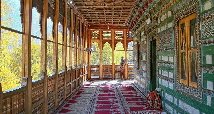 Couloir en bois coloré avec des tapis à motifs à l'intérieur du palais de Khaplu donnant sur des arbres d'automne.