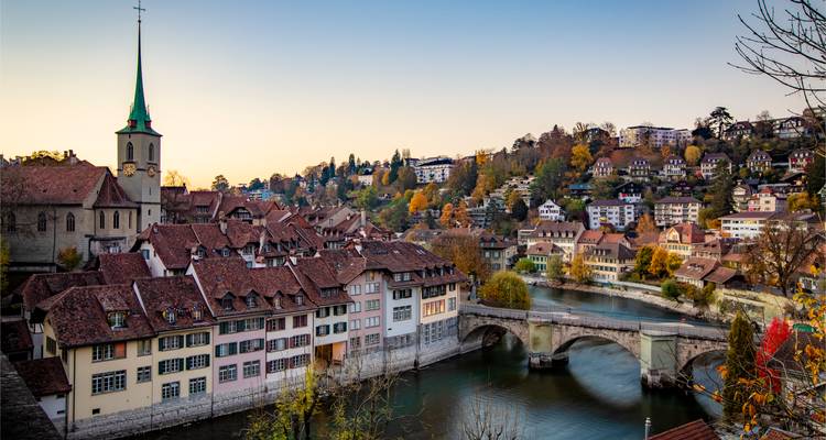 Bezaubernder Herbstblick über Berns Altstadtdächer aus rotem Ziegel und die gewölbte Steinbrücke, die den smaragdgrünen Fluss überspannt.