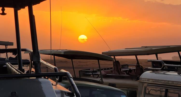 Vehículos de safari estacionados con escotillas del techo abiertas mientras el sol se pone en un cielo polvoriento