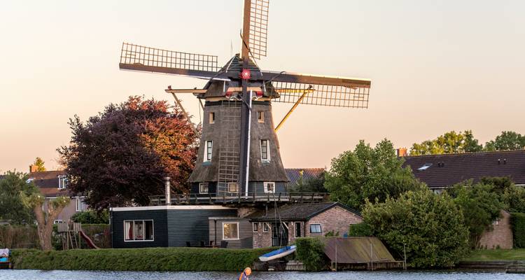 Classic Dutch windmill on a tranquil canal at dusk with village houses in the background.