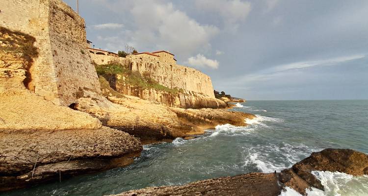 Golden-lit medieval castle walls sit atop rugged coastal rocks as waves crash below in Ulcinj.