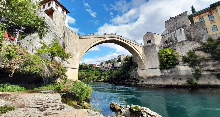 Vista de ángulo bajo del elegante arco del Stari Most que cruza el río Neretva color turquesa con el casco antiguo de Mostar detrás.