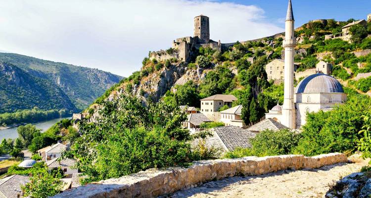 Un sendero de piedra conduce pasando una mezquita con cúpula hacia las murallas de una fortaleza medieval encaramadas en una cresta rocosa en Počitelj.