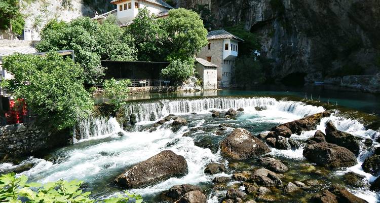 El agua espumosa del río se precipita sobre cascadas junto al histórico monasterio Blagaj Tekke sombreado por árboles.