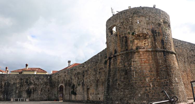 Round stone watchtower and fortress walls of Ulcinj Old Town under a cloudy sky.