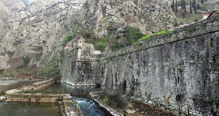 Long defensive stone wall hugging a rocky gorge with water channels at its base.