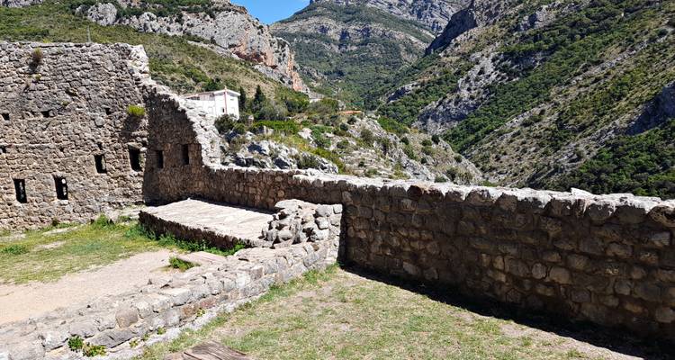 Stone wall segment of a hilltop fortress overlooking a steep rocky valley under clear skies.