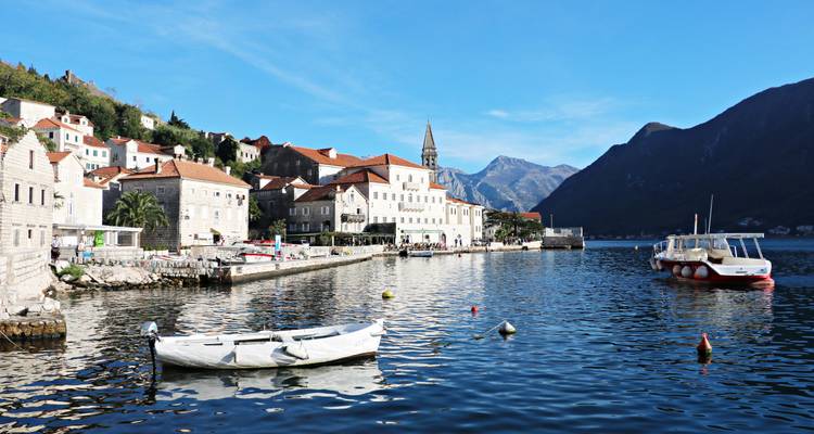 Charming stone village of Perast with terracotta rooftops lining a tranquil bay, backed by towering Montenegrin mountains and small boats.