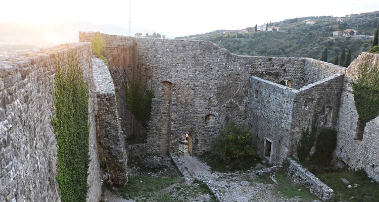Interior courtyard of an ancient stone fortress with creeping ivy and soft setting sun.