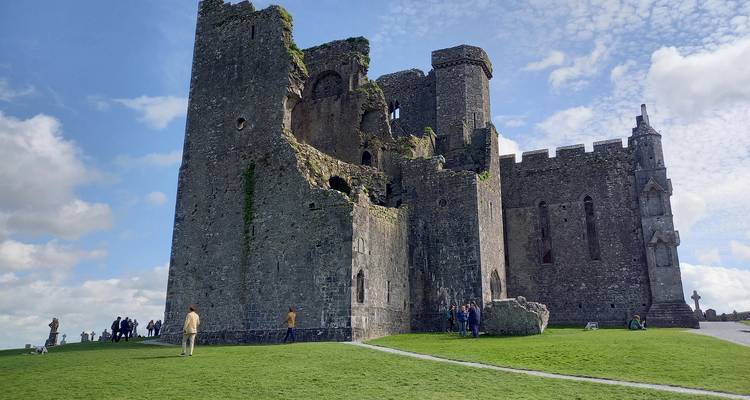 Ruines du complexe du château du Rocher de Cashel situé sur une colline herbeuse sous un ciel bleu.