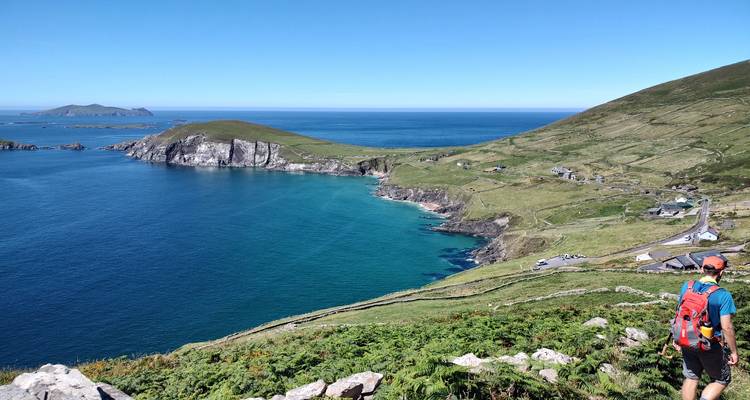 Randonneur avec sac à dos contemplant l'Atlantique bleu profond depuis un sentier côtier en hauteur.