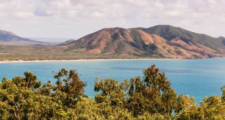 Bahía azul bordeada por eucaliptos y colinas marrones escarpadas en la Península del Cabo York.