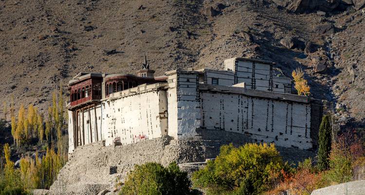 Fort historique en pierre perché sur une pente rocheuse entouré de feuillage d'automne sous un ciel dégagé.