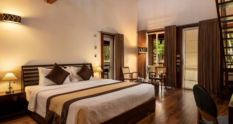 Gemütliches Hotelzimmer mit Kingsize-Bett, Holzparkett und Balkontüren, die zum Grünen hinausgehen.