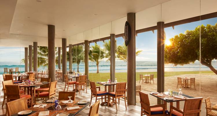 Restaurant am Meer mit Glaswänden mit Blick auf einen von Palmen gesäumten Strand zur goldenen Stunde.
