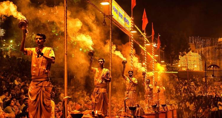 Des prêtres effectuent le rituel de Ganga Aarti en tenant des lampes flamboyantes parmi la fumée et les lumières dorées devant une foule.