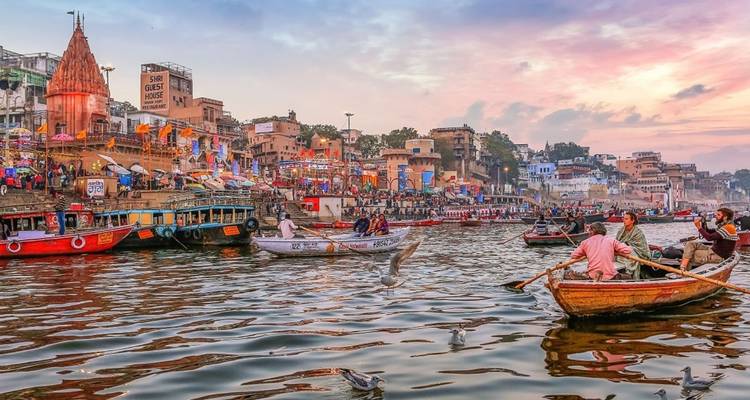 Scène animée de lever de soleil sur les ghats de Varanasi avec des bateaux, des temples, des pèlerins et des mouettes qui volent le long du Gange.