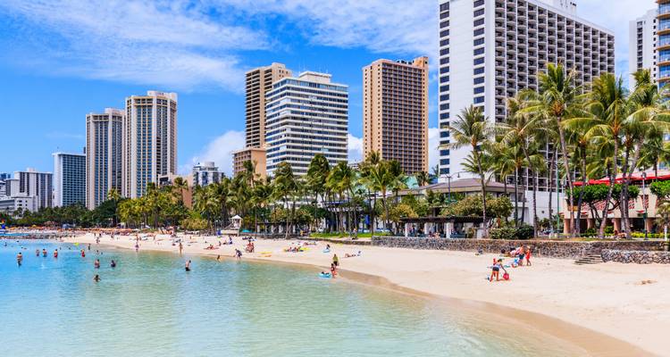 Eaux turquoise calmes et peu profondes de Waikiki avec des vacanciers et d'imposantes tours d'hôtel.