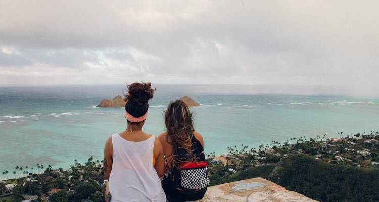 Deux amis sont assis sur un point de vue côtier contemplant le vaste océan turquoise et les petits îlots.