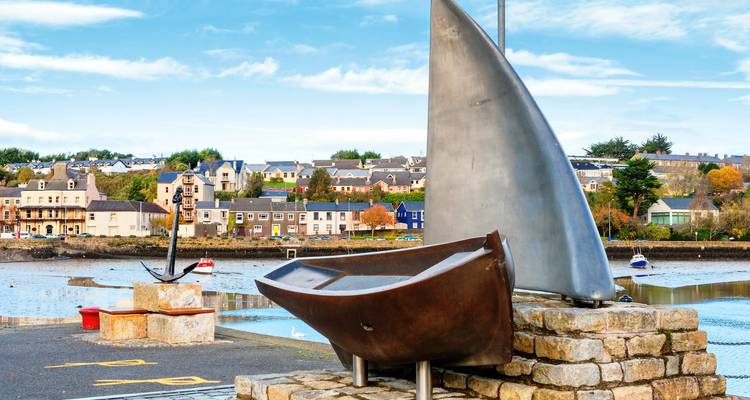 Escultura del malecón de un velero y ancla de metal con casas coloridas del pueblo costero detrás.