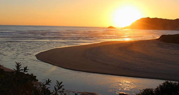 Le soleil doré se couche sur un lagon de plage tranquille qui s'incurve vers l'horizon océanique.