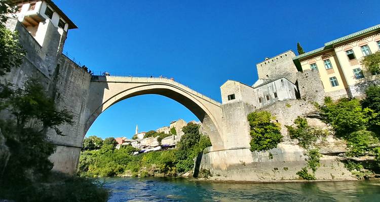 The iconic stone arch of Mostar’s Stari Most spans the Neretva River against a cloudless deep blue sky.