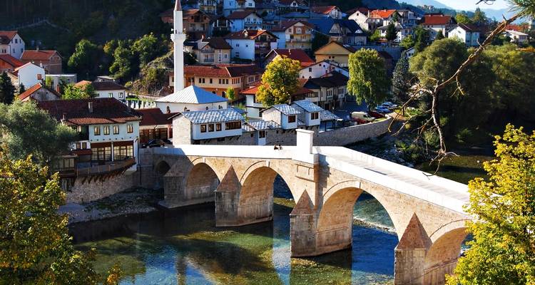 An elegant multi-arch Ottoman bridge spans a crystal river amid a leafy Bosnian town.