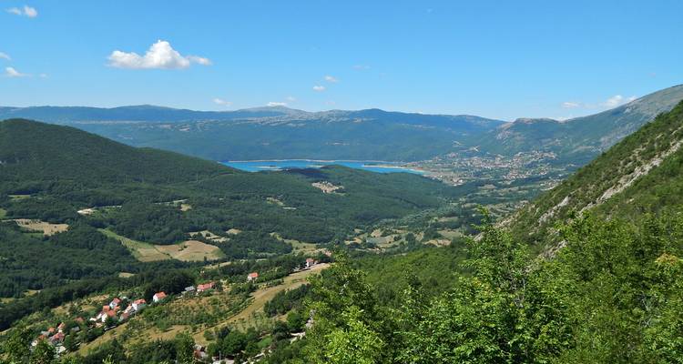Vue panoramique d'une large vallée avec des forêts en mosaïque, des villages et un réservoir bleu au loin encadrés par des crêtes montagneuses.