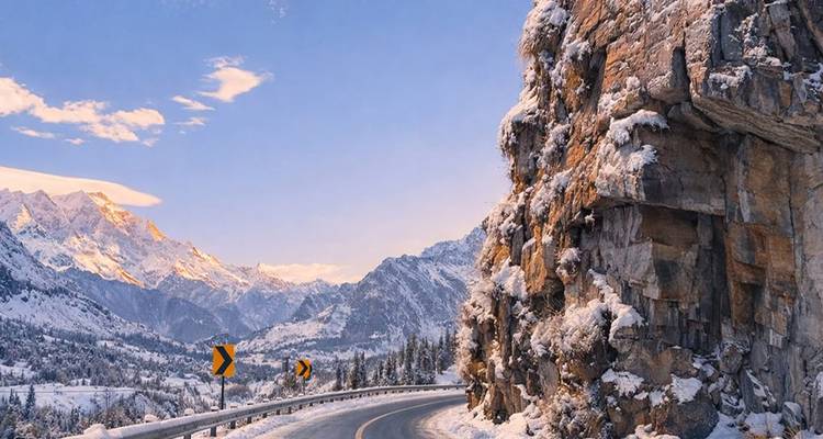 Serpenteante carretera de montaña bordeada por acantilados nevados y picos distantes del Himalaya
