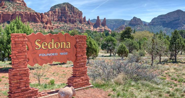 Panneau rustique en pierre annonçant Sedona avec des flèches de roche rouge et de la végétation désertique en arrière-plan.