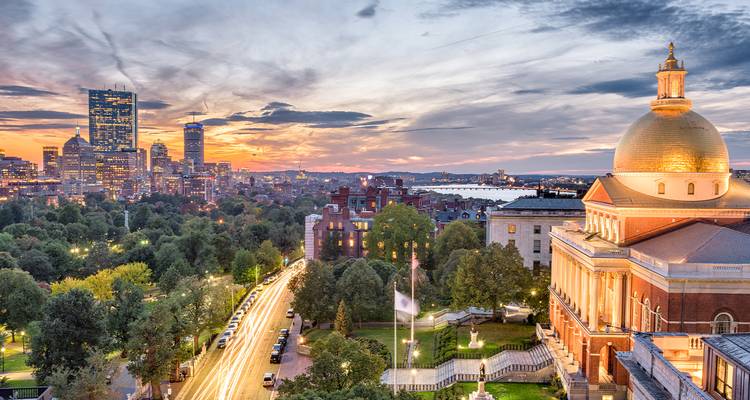 Bostons Skyline in der Dämmerung mit der Kuppel des State House und Lichtspuren entlang der von Bäumen gesäumten Allee.