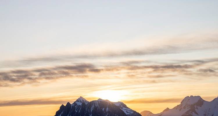 Soleil se levant derrière les pics antarctiques enneigés sous un ciel doré.