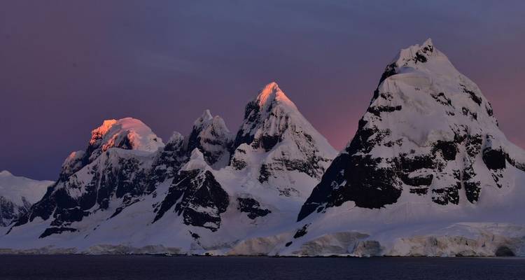 Chaîne de montagnes antarctique déchiquetée baignée dans la lueur rosée du crépuscule.