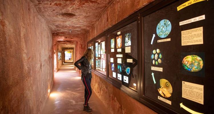 Un visiteur observe des présentations colorées de minéraux dans un tunnel souterrain de musée d'opale.