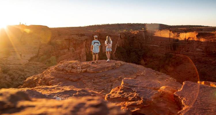Deux voyageurs se tiennent sur un éperon rocheux à l'heure dorée, surplombant un canyon rouge profond.