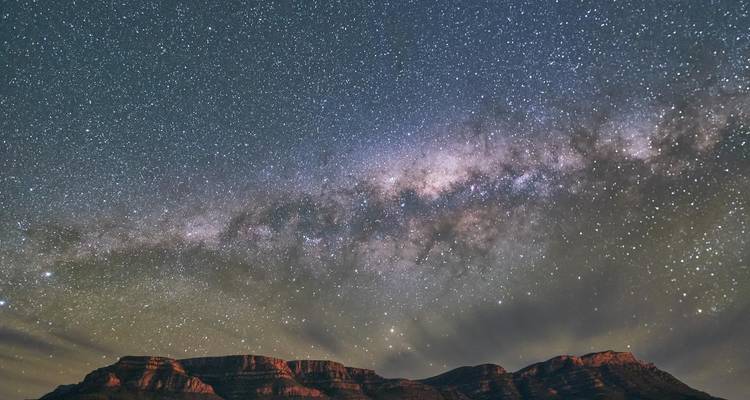 Ciel nocturne étoilé et Voie lactée s'arquant au-dessus des chaînes de montagnes désertiques aux silhouettes sombres.