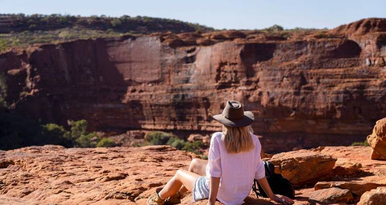 Femme au chapeau se détend sur un rebord de grès rouge surplombant un profond canyon de l'arrière-pays.