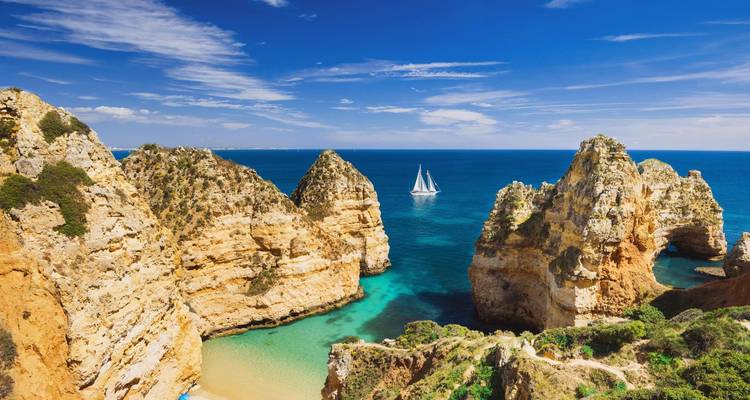 Acantilados marinos dorados y escarpados de Ponta da Piedade se elevan desde las aguas turquesas del Atlántico con un velero a lo lejos.