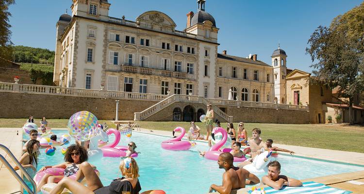 Jóvenes viajeros chapotean con inflables coloridos en la piscina de un castillo en la campiña francesa.